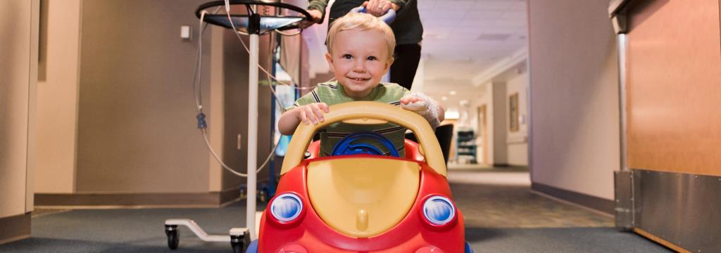 Child Life and Expressive Therapies / boy in a play mobile car smiling 