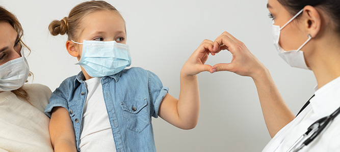 Image of pediatric patient wearing a mask and making a heart with her hand.